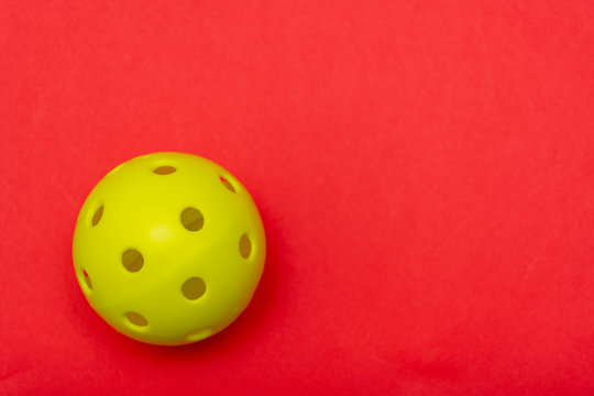 Bright yellow pickleball or whiffle ball on a solid bright red flat lay background symbolizing sport